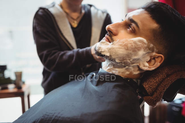 Мужчине сбривают бороду в парикмахерской — стоковое фото