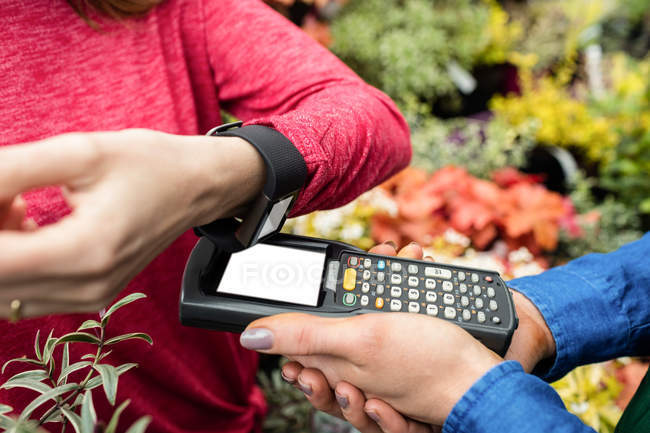 Cropped image of Woman making payment through smart watch in garden centre — Stock Photo