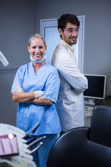 Портрет улыбающегося стоматолога и ассистента стоматолога, стоящего спиной к спине в стоматологической клинике — стоковое фото