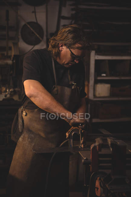 Blacksmith working on metal at work shop — Stock Photo