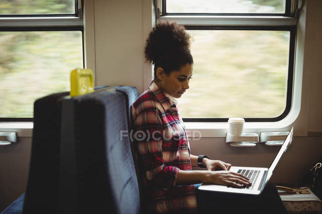 Mujer joven usando el ordenador portátil mientras está sentado en el tren - foto de stock