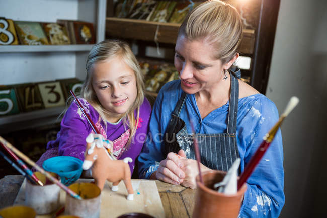 Женщина-гончар помогает девушке в живописи в мастерской по гончарному делу — стоковое фото