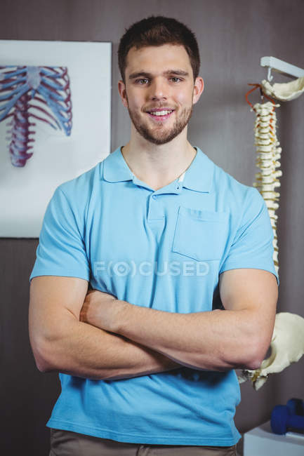Porträt eines männlichen Physiotherapeuten, der mit verschränkten Armen in der Klinik steht — Stockfoto