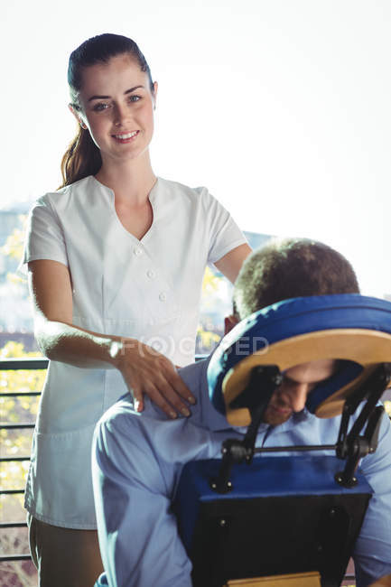 Retrato de fisioterapeuta femenina dando masaje de espalda a paciente masculino en clínica - foto de stock