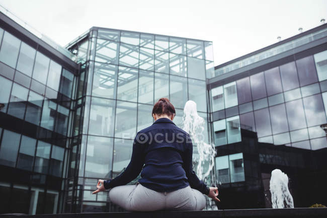 Вид ззаду бізнес-леді робить йогу проти офісної будівлі — стокове фото