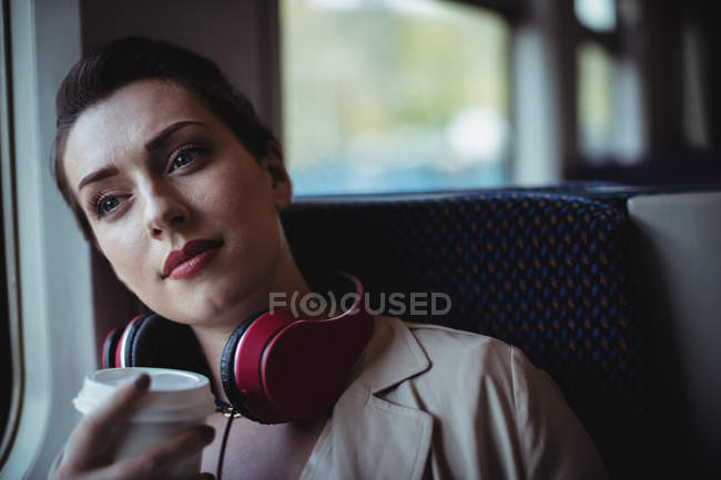 Mulher bonita pensativo segurando copo descartável no trem — Fotografia de Stock