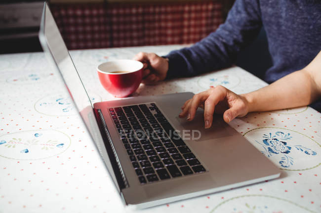 Imagen recortada de la pareja usando el ordenador portátil mientras toma café en casa - foto de stock