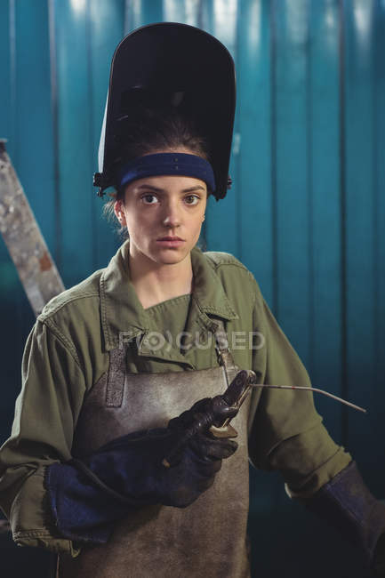 Retrato del soldador femenino sosteniendo arco de soldadura en taller - foto de stock