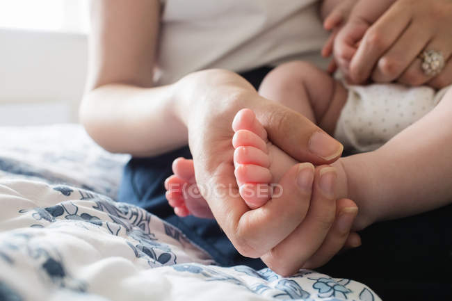 Image recadrée de mère tenant des pieds de bébé sur le lit dans la chambre à coucher à la maison — Photo de stock
