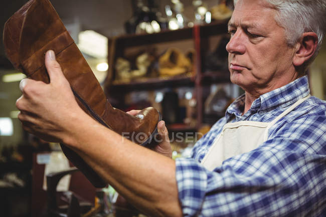 Зрелый сапожник осматривает обувь в мастерской — стоковое фото