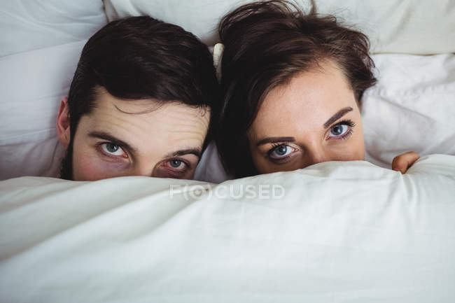 Portrait of happy couple covering faces by blanket and having fun in bedroom at home — Stock Photo