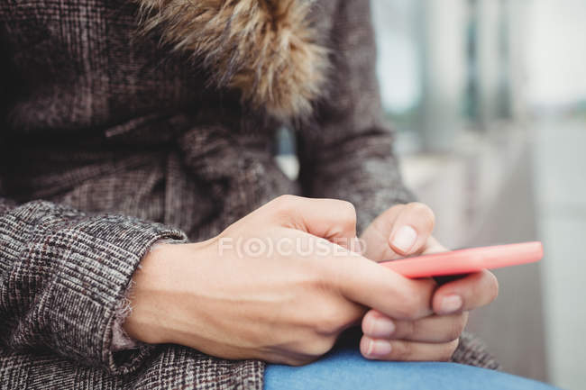 Sección media de la mujer con el teléfono mientras está sentado al aire libre - foto de stock