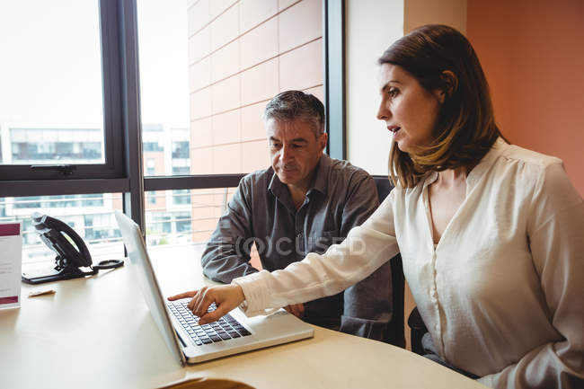 Femme discutant avec un collègue sur un ordinateur portable au bureau — Photo de stock