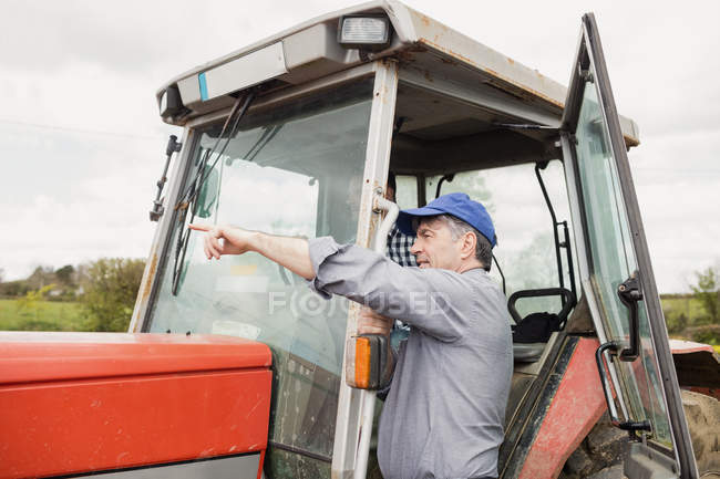 Фермер вказує, стоячи на тракторі на полі — стокове фото