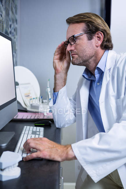 Dentista atencioso trabalhando no computador na clínica odontológica — Fotografia de Stock