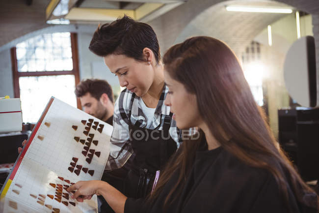 Mulher selecionando a cor do cabelo com estilista no salão de cabeleireiro — Fotografia de Stock