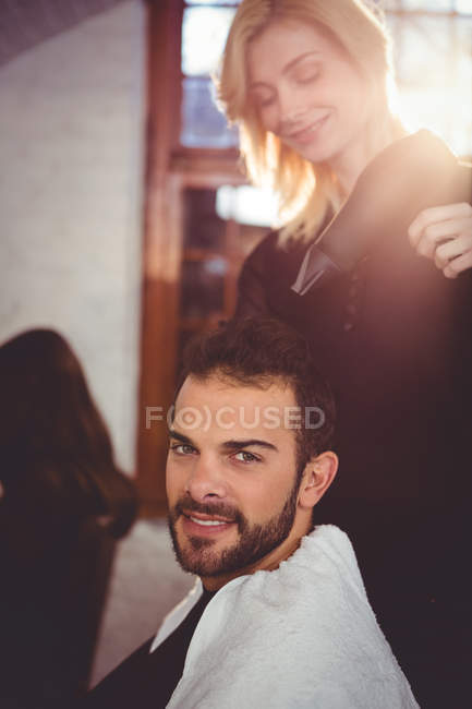 Retrato del hombre sonriente secándose el pelo con secador de pelo en el salón - foto de stock