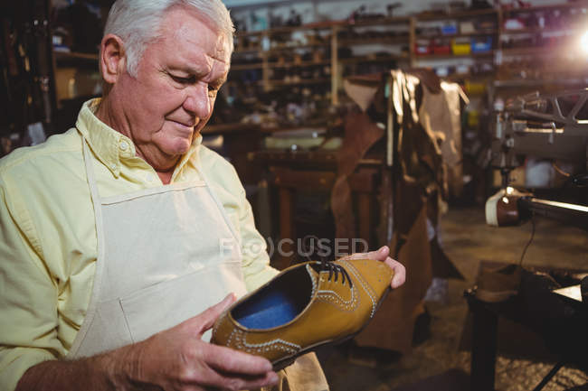 Thoughtful shoemaker examining a shoe in workshop — Stock Photo
