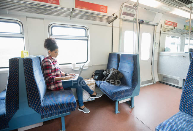 Toute la longueur de la femme en utilisant un ordinateur portable tout en étant assis dans le train — Photo de stock