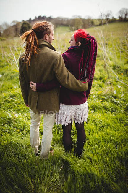 Rear view of young couple with arm around while standing on grassy field in park — Stock Photo