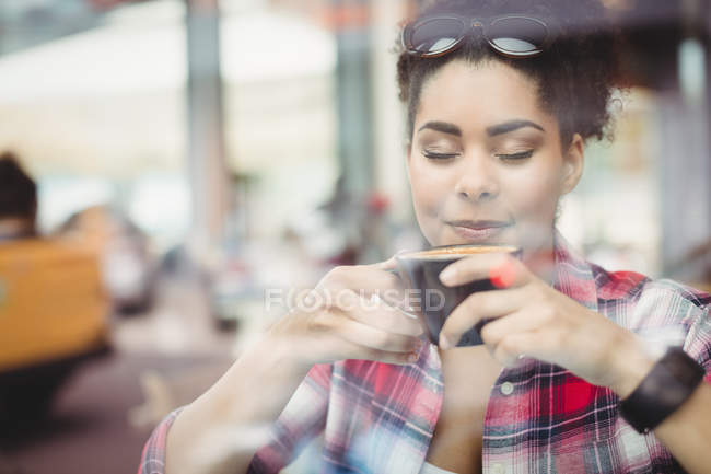 Primer plano de la joven con los ojos cerrados mientras toma café en el restaurante - foto de stock