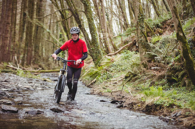 Front view of biker walking with bicycle in stream at forest — Stock Photo