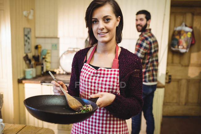 Жінка приготування їжі на кухні, в будинку з чоловіком у фоновому режимі — стокове фото