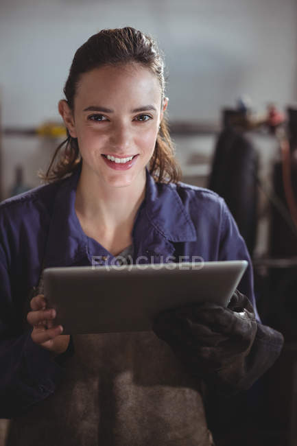 Portrait of female welder holding digital tablet in workshop — Stock Photo