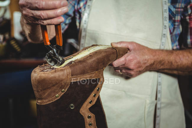 Sección media del zapatero reparando un zapato en el taller - foto de stock