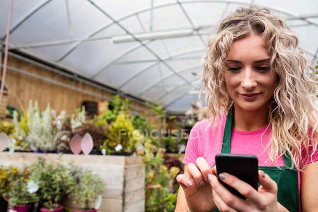 Жіночий флорист, використовуючи мобільний телефон в садовому центрі — стокове фото