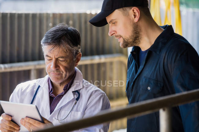 Vet and farm worker looking in tablet computer at barn — Stock Photo