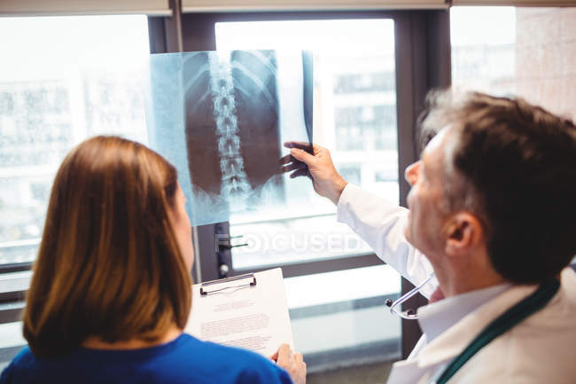 Vista posterior del médico examinando rayos X mientras la enfermera escribe en el portapapeles en el hospital - foto de stock