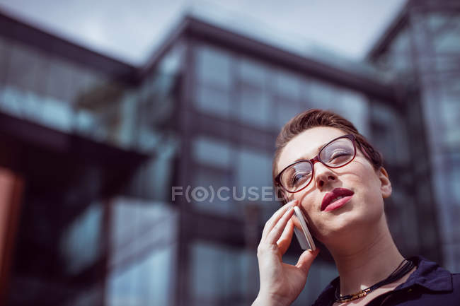 Tiefansicht einer jungen Frau, die mit dem Handy gegen ein Gebäude spricht — Stockfoto