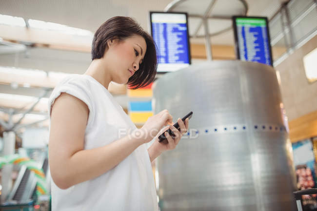 Pasajera que usa teléfono móvil en la terminal del aeropuerto - foto de stock