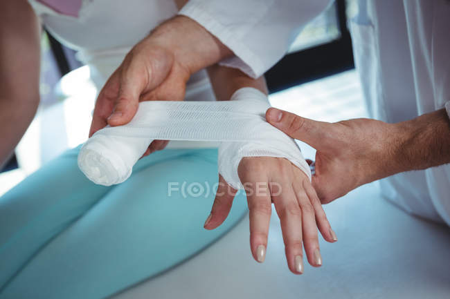 Imagen recortada del terapeuta masculino poniendo vendaje en la mano del paciente femenino en la clínica - foto de stock