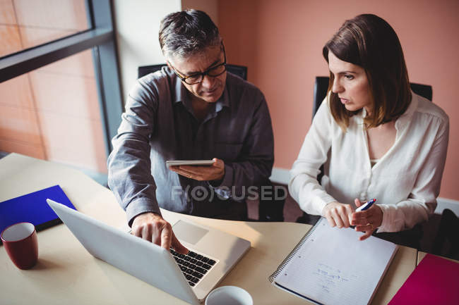 Мужчина и женщина обсуждают за цифровым планшетом и ноутбуком в офисе — стоковое фото