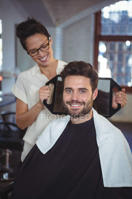 Coiffeuse souriante montrant à l'homme sa coupe de cheveux dans un miroir au salon — Photo de stock
