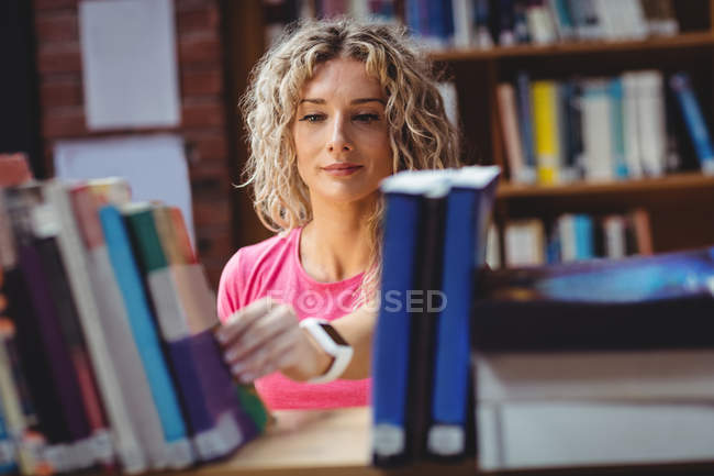 Mujer quitando libro de la estantería en la biblioteca - foto de stock