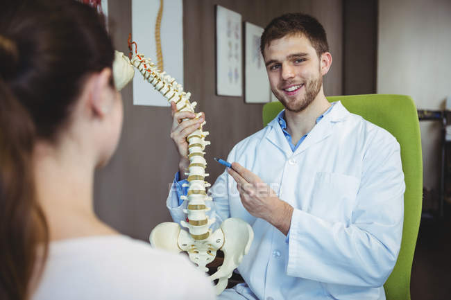 Retrato de fisioterapeuta explicando coluna vertebral para paciente do sexo feminino na clínica — Fotografia de Stock
