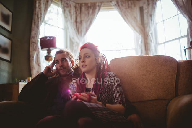 Jovem casal assistindo televisão enquanto sentado no sofá em casa — Fotografia de Stock