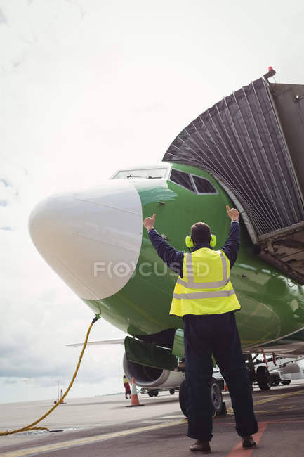 Vista trasera del trabajador de la tripulación de tierra del aeropuerto dirigiendo el avión en la pista - foto de stock