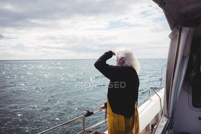 Vista laterale del pescatore in piedi sulla barca e guardando il mare — Foto stock