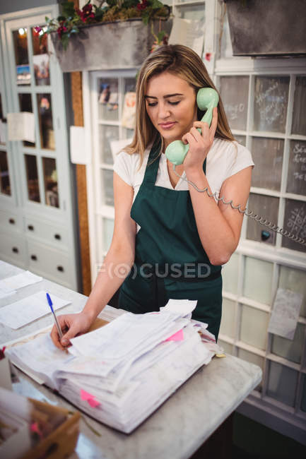 Floristería femenina comprobando facturas mientras habla por teléfono en la floristería - foto de stock