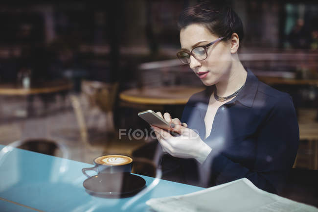Молода жінка використовує мобільний телефон у кафе, який видно через скло — стокове фото