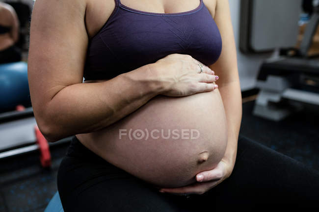 Средняя секция беременной женщины, сидящей на мяче в спортзале — стоковое фото