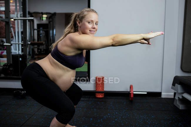 Retrato de la mujer embarazada realizando ejercicio de estiramiento en el gimnasio - foto de stock