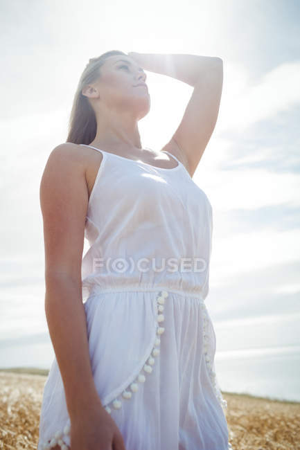Vista basso angolo di donna con mano nei capelli in piedi nel campo di grano nella giornata di sole — Foto stock