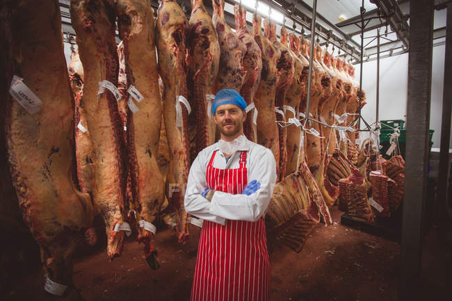 Portrait de boucher debout avec les bras croisés dans la salle de stockage de viande à la boucherie — Photo de stock