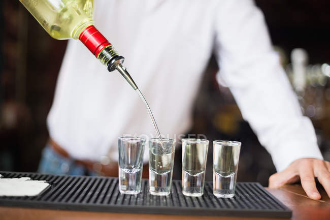 Close-up de bartender derramando tequila em copos de tiro no balcão de bar no bar — Fotografia de Stock