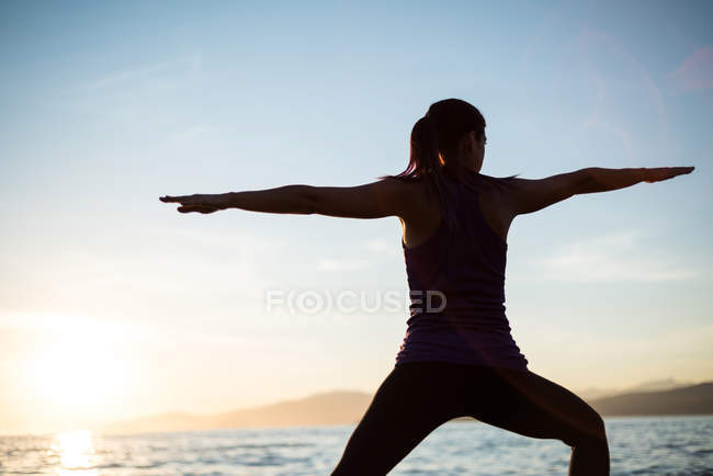 Vista posteriore di donna che esegue yoga sulla spiaggia durante il tramonto — Foto stock